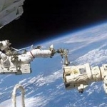 L’homme et le robot travaillant pied dans la pince. L’astronaute Jerry Ross flotte au-dessus de l’atmosphère terrestre, attaché à une extrémité du bras robotique Canadarm2