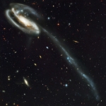 La  «galaxie du têtard», UGC 10214, sur fond de galaxies primordiales. Profondeur de champ : 12,5 milliards d’années... Les zones bleutées dans le bras détaché de la galaxie correspondent à des zones de formation d’étoiles, engendrées par l’onde de choc de la collision.