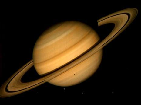 Saturne vue depuis une distance de 21 millions de kilomètres en 1981 par la sonde Voyager 2. C\'est une image en vraies couleurs. On peut voir quatre des satellites de Saturne : Téthys, Dioné, Rhéa, et (moins évident à repérer) Mimas. L\'ombre portée sur la planète est celle de Téthys. 